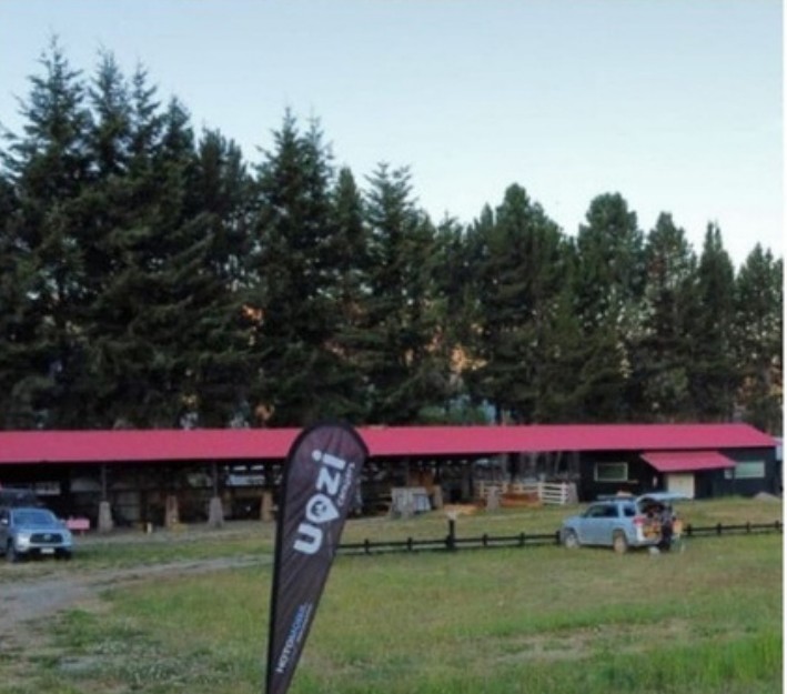 Los sitios del RV Park con el galpón techado de techo rojo, araucarias detrás y un vehículo estacionado.